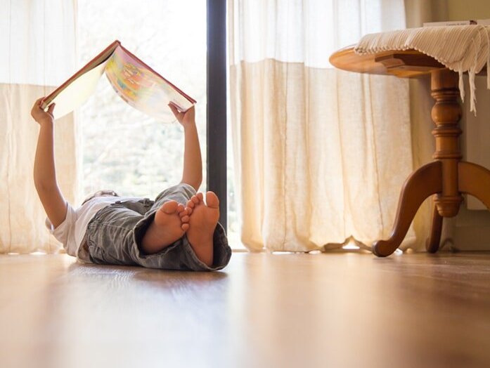 Child reading book on hardwood floor